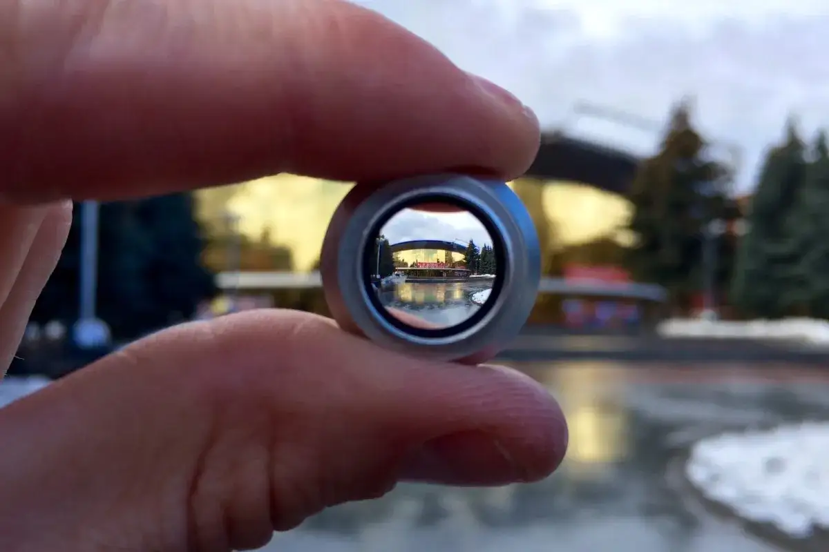 Widok przez soczewkę na budynek z podświetlanym logo. Zbliżenie ukazuje pogorszenie jakości zdjęć w telefonie, gdy próbujemy uchwycić detale.