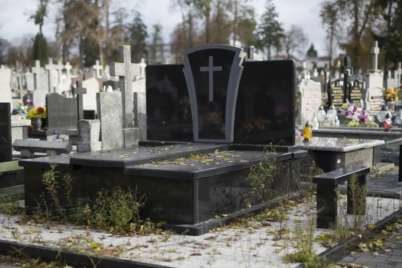 Nagrobek z czarnego granitu na cmentarzu, pokryty opadłymi liśćmi.