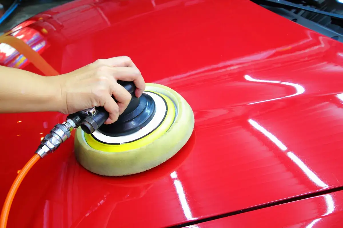 Dłoń trzymająca polerkę samochodową na czerwonym lakierze.
