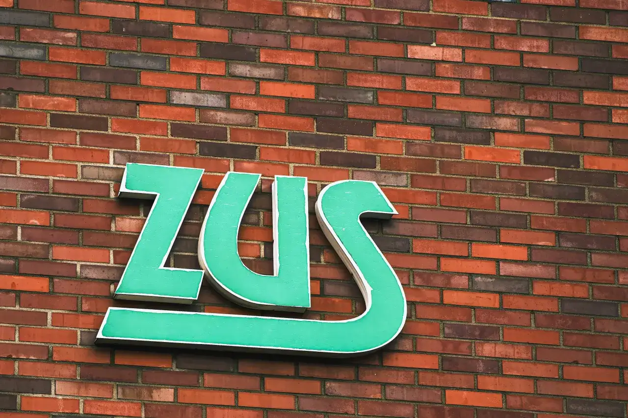 Zielone litery ZUS na ceglanej ścianie.
