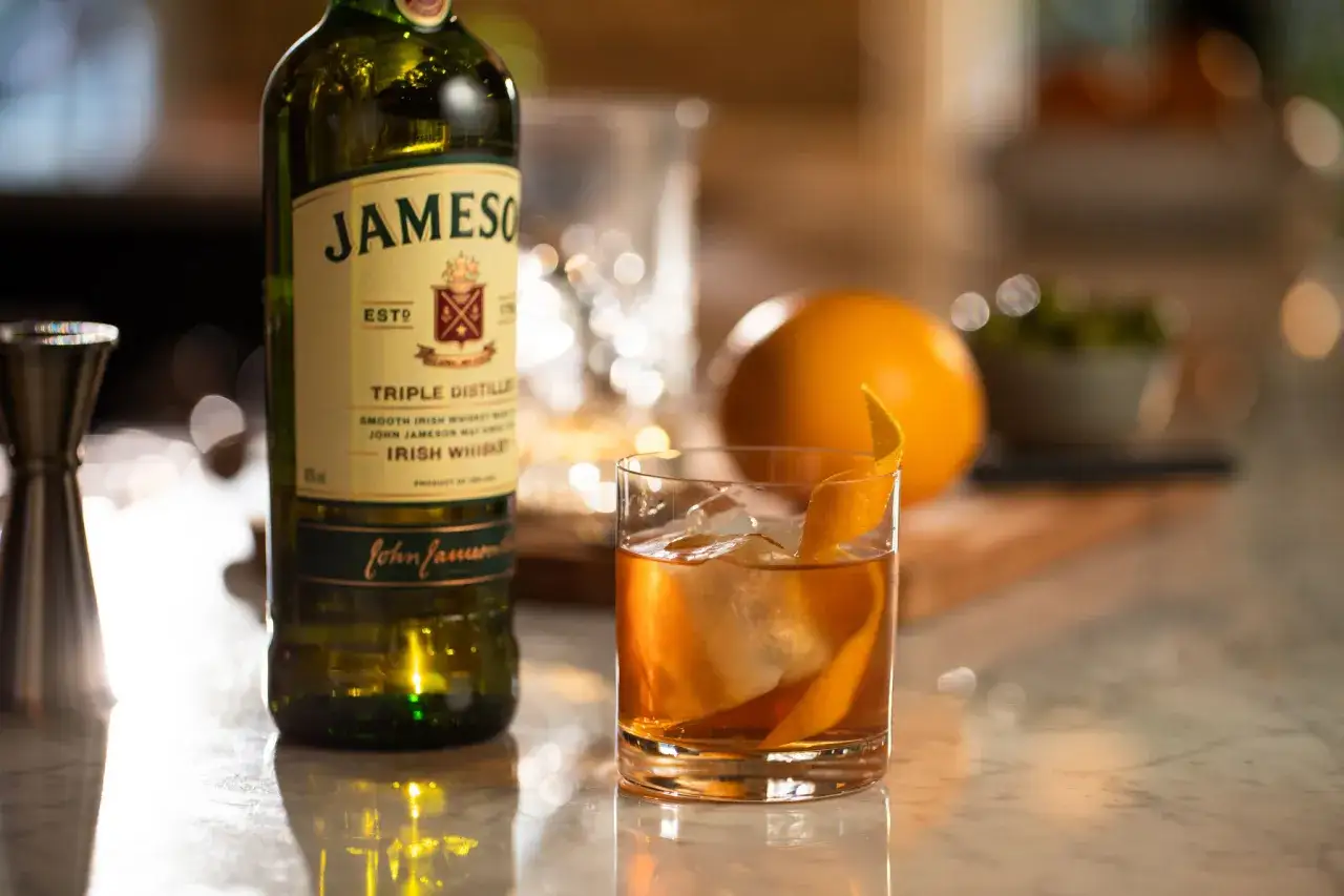 Klasyczny Old Fashioned na bourbonie czy na żytniej whisky? Obok butelka Jameson, szklanka z drinkiem i pomarańcza.