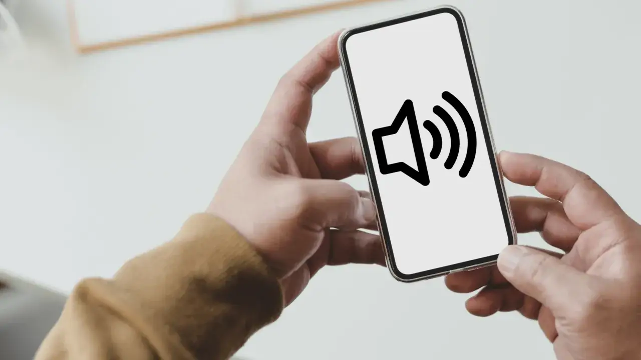 Dłoń trzyma smartfon z ikoną głośnika na ekranie.