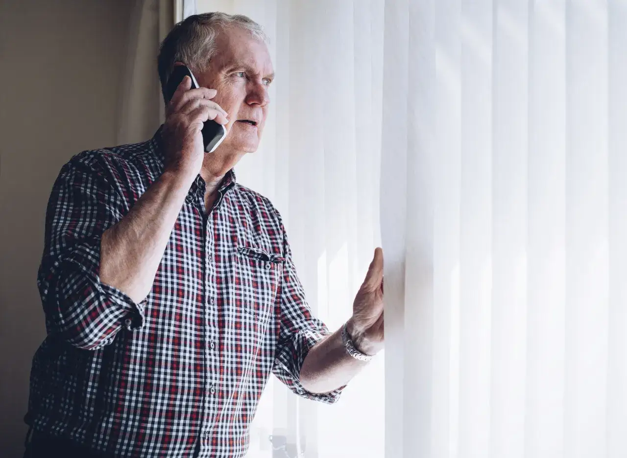 Zaniepokojony starszy mężczyzna rozmawia przez telefon, szukając informacji, gdzie zgłosić zaniedbywanie osoby starszej.