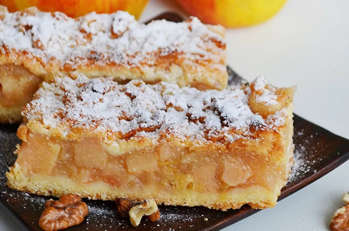 Dwa kawałki szarlotki posypane cukrem pudrem, z widocznymi jabłkami i orzechami. To szarlotka najlepsza jaką jadłam!