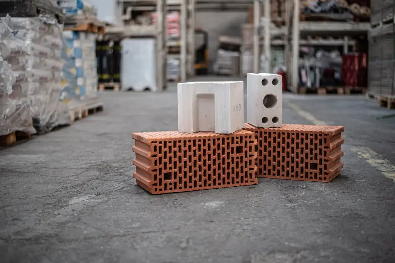 Cegły ceramiczne i białe pustaki na betonowym podłożu. Zastanawiasz się, ile cegieł na metr kwadratowy potrzebujesz do budowy?