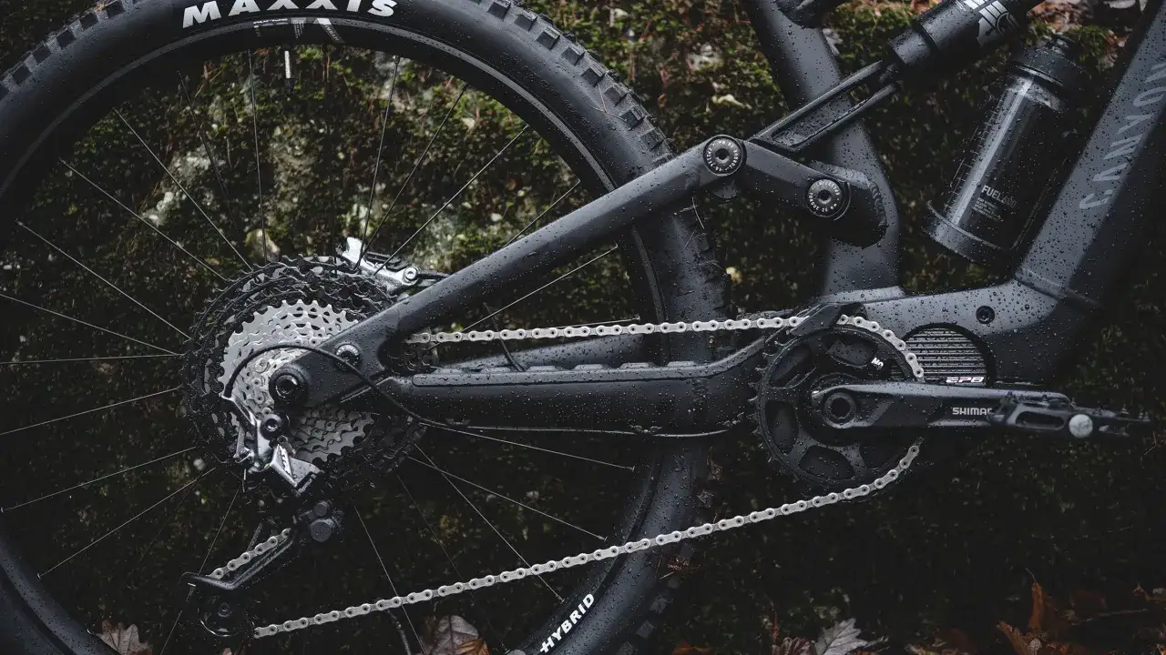 Część roweru elektrycznego z napędem **Shimano EP8** w deszczu. Widoczna kaseta, przerzutka, łańcuch i korba.