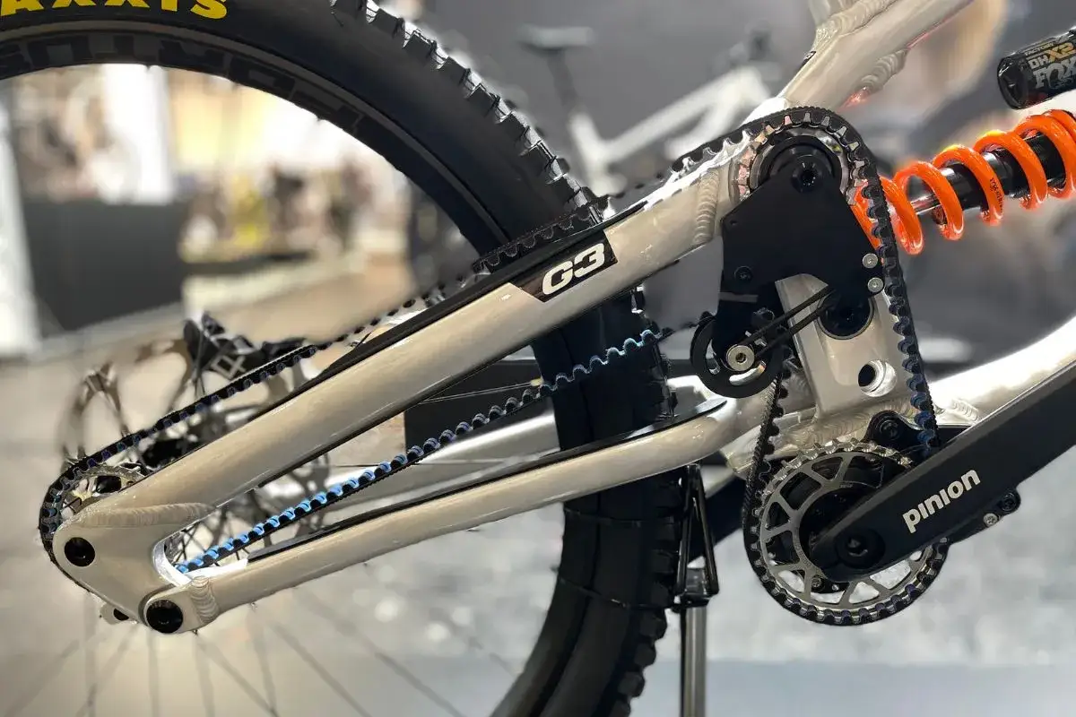 Szara rama roweru z napędem na pasek z niebieskimi akcentami. Widoczny amortyzator Fox DHX2.