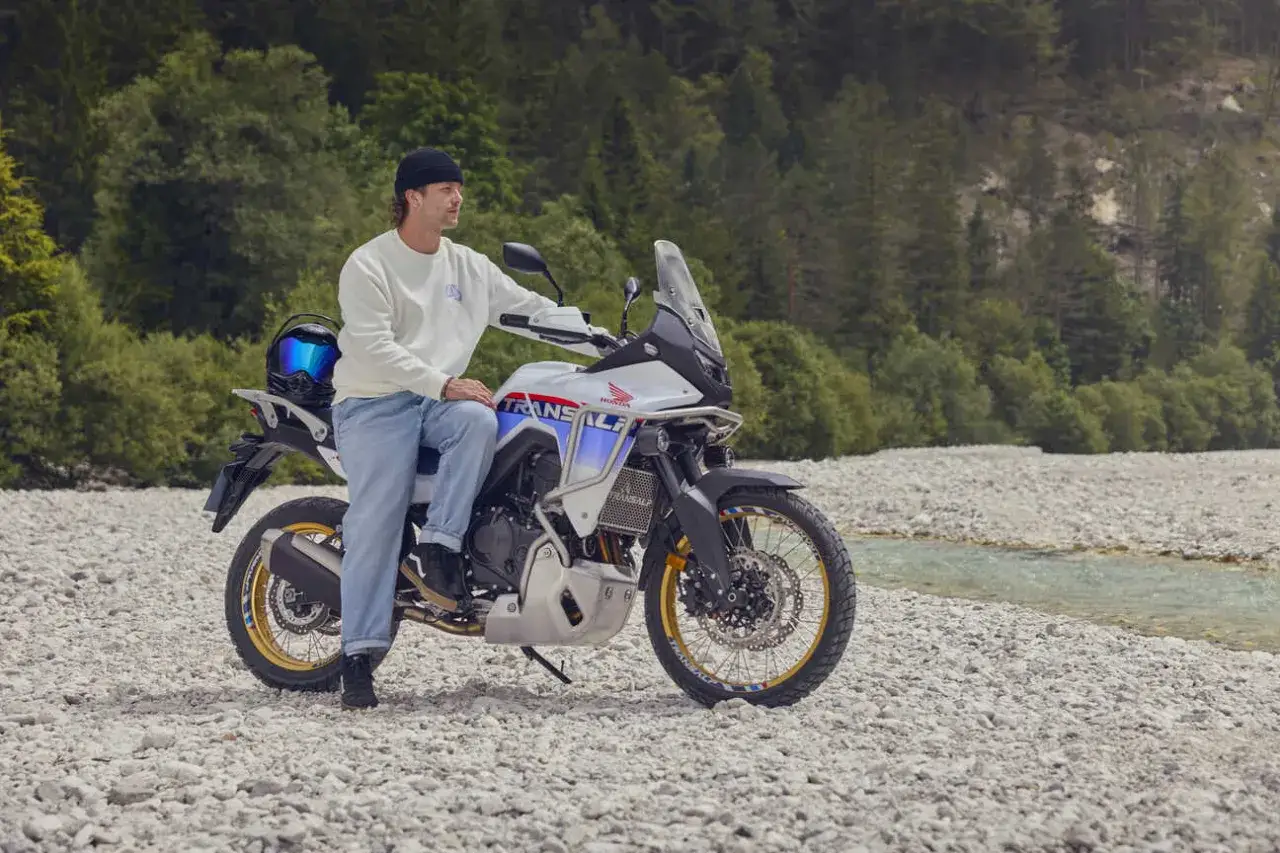 Mężczyzna na motocyklu Honda Transalp, gotowy na przygodę motocyklem po Europie. W tle las i strumień.
