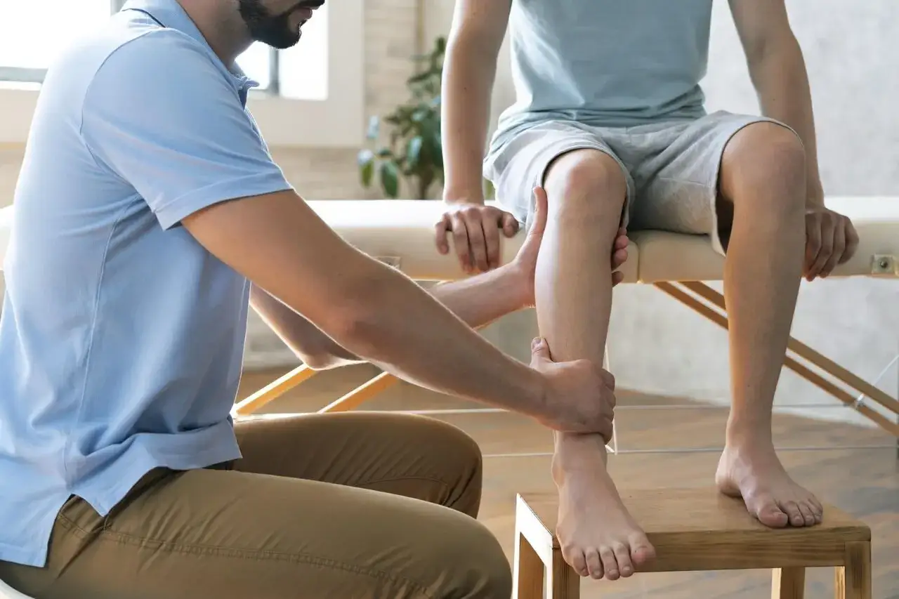 Fizjoterapeuta pomaga w domowej rehabilitacji stawu skokowego, delikatnie masując nogę pacjenta.