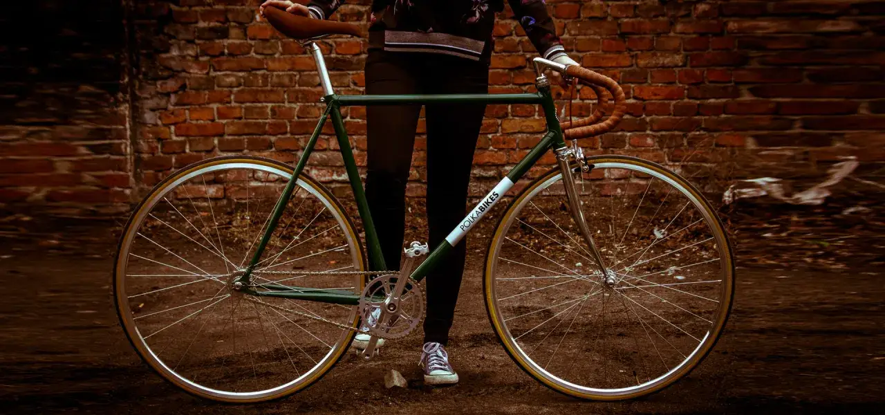 Zielony rower z brązowym siodełkiem i kierownicą, stojący przy ceglanej ścianie. To jest rower, który zaprasza do jazdy.