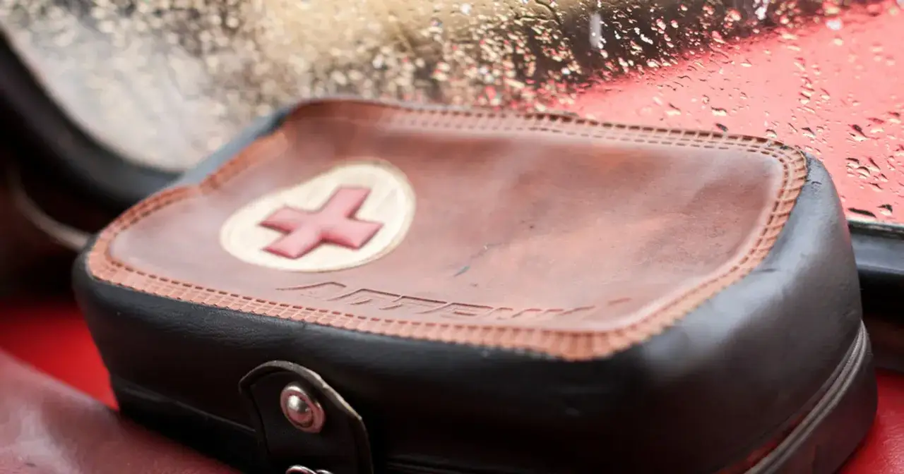 Brązowa apteczka samochodowa z czerwonym krzyżem na tle deszczowej szyby.