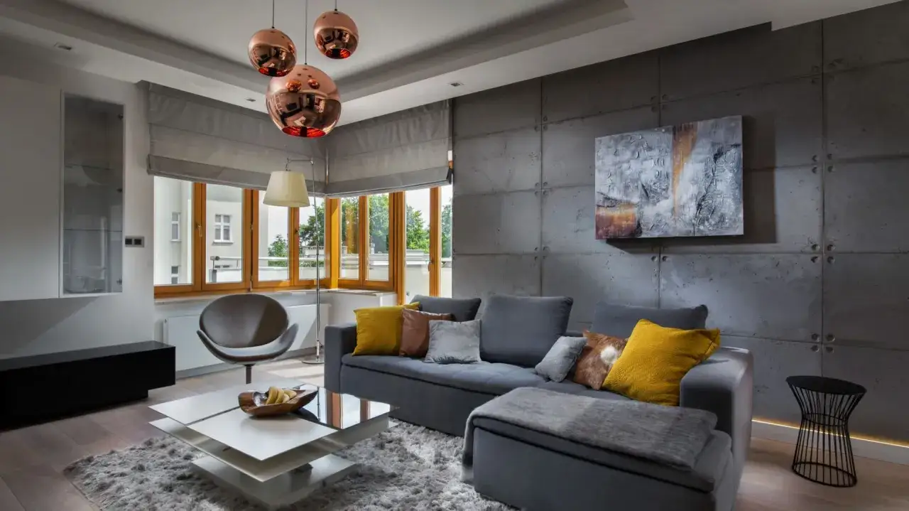 Nowoczesny salon z betonową ścianą. Inspiracje dla odważnych: szara sofa, miedziane lampy i geometryczne meble tworzą industrialny klimat.