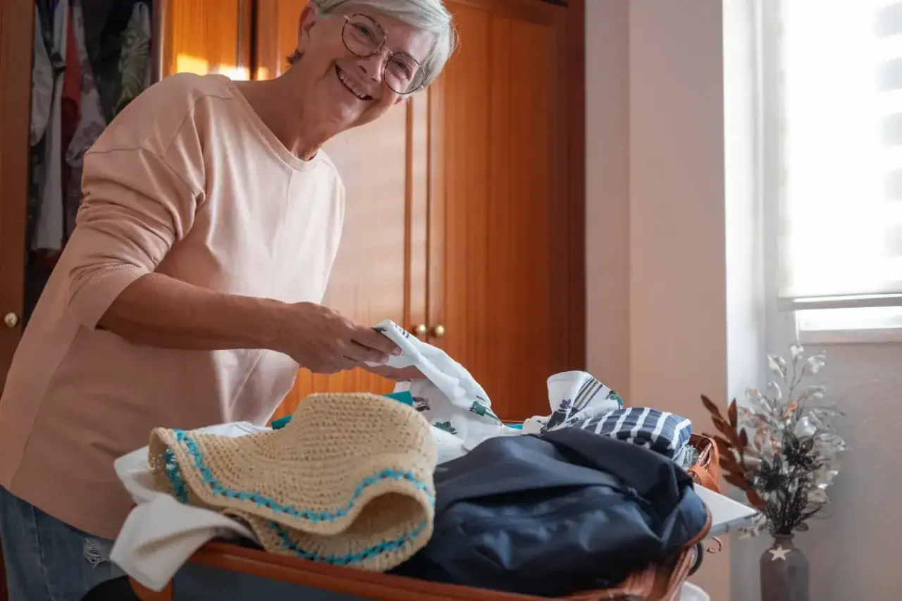 Uśmiechnięta starsza pani pakuje walizkę. To może być początek przygotowań, jak załatwić dom opieki dla starszej osoby.