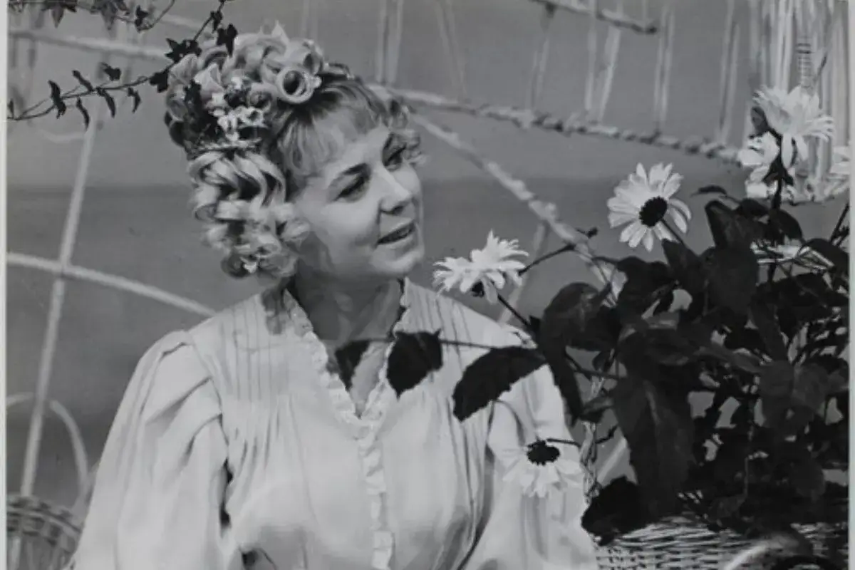 Ilona Stawińska w kwiecistej fryzurze i jasnej sukni, otoczona kwiatami, wygląda jak z baśni.