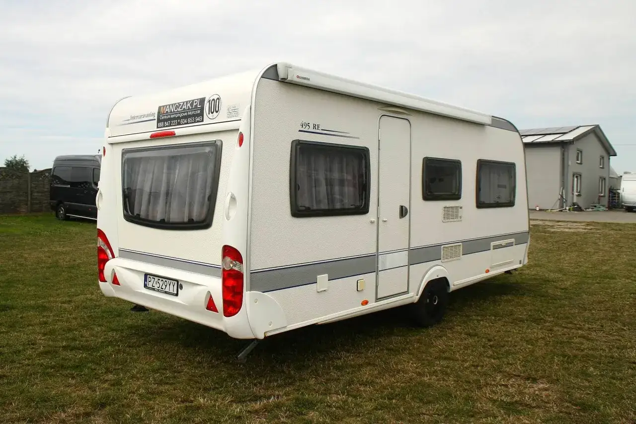 Biała przyczepa kempingowa Caravelair 495 RE na trawie, z widocznym logo MANCZAK.PL.