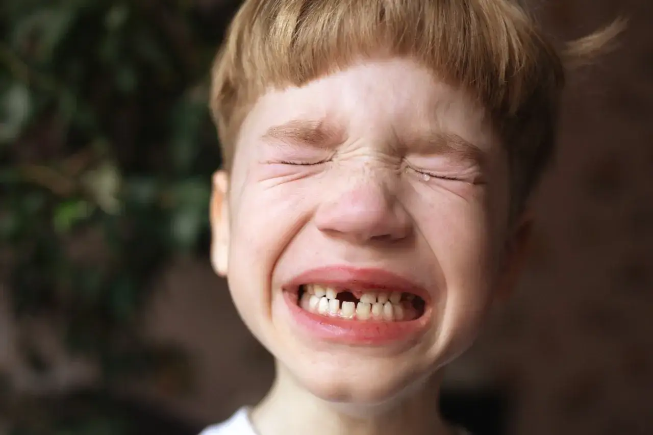 Chłopiec płacze, widać ukruszony ząb mleczny. Łzy spływają po policzkach.