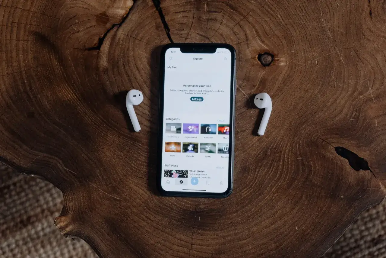 Telefon z aplikacją "Explore" i słuchawki AirPods leżące na drewnianym blacie. Dowiedz się, jak podłączyć AirPods do telefonu.