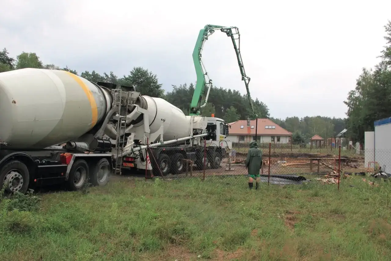 Betoniarka z pompą przygotowuje jaki beton na strop. Na placu budowy widać dom w tle i pracownika w zielonej kurtce.