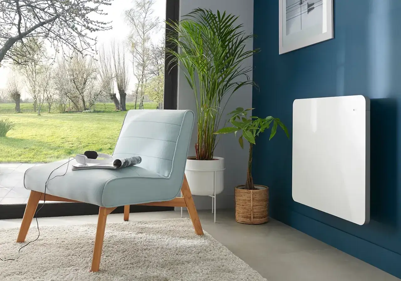 Nowoczesny, biały grzejnik elektryczny na granatowej ścianie. Idealny jako jaki grzejnik do pokoju 10m2, obok jasnoniebieskiej kanapy i roślin.