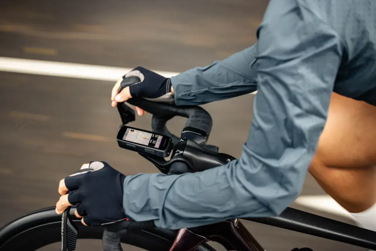 Kolarz z rękawiczkami na kierownicy, na której zamontowany jest nawigator Hammerhead Karoo 3 z mapą trasy.