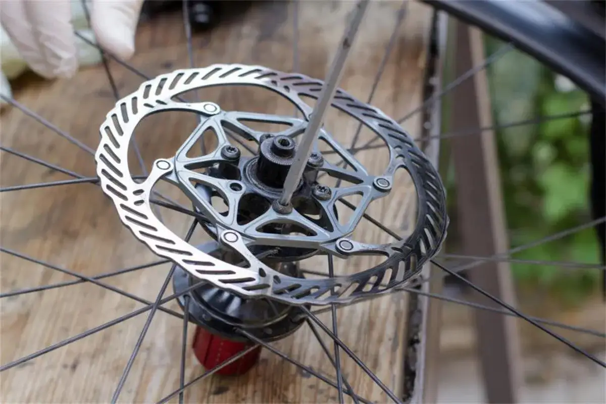 Rękawiczka i śrubokręt podczas czyszczenia tarcz hamulcowych roweru.