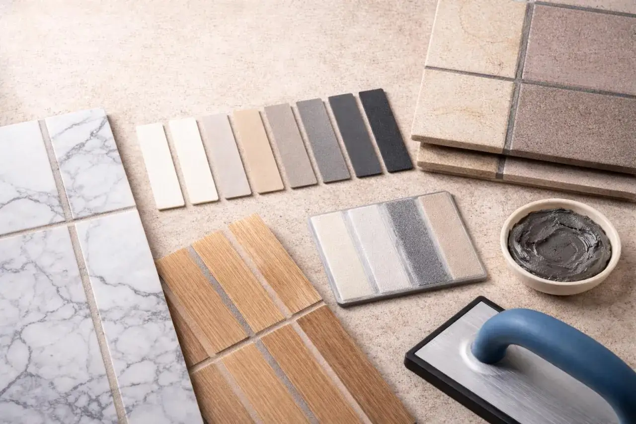 Próbki płytek, paleta kolorów fug, kielnia i miska z masą fugową.