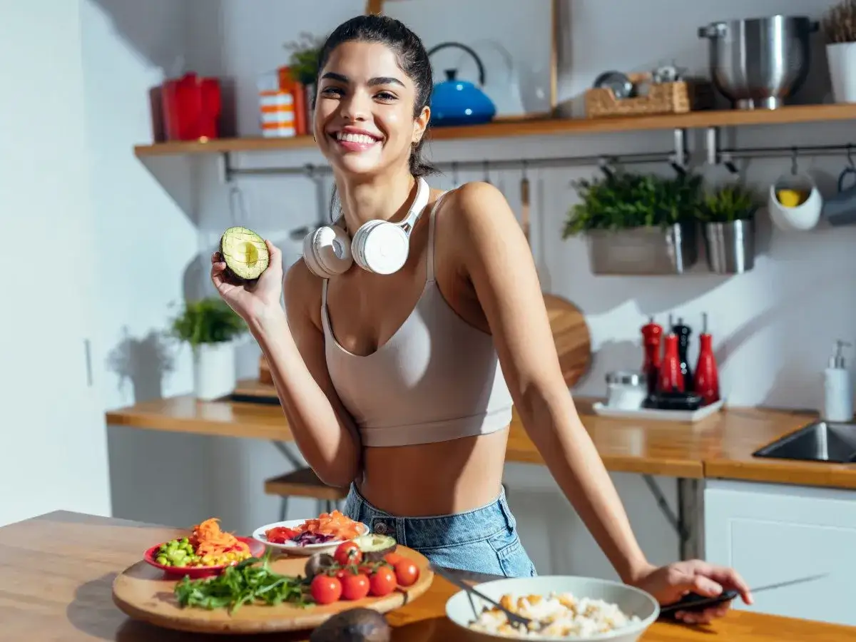 Uśmiechnięta kobieta z awokado w dłoni, przygotowująca posiłki. To inspiracja na dietę odchudzającą dla leniwych jadłospis.