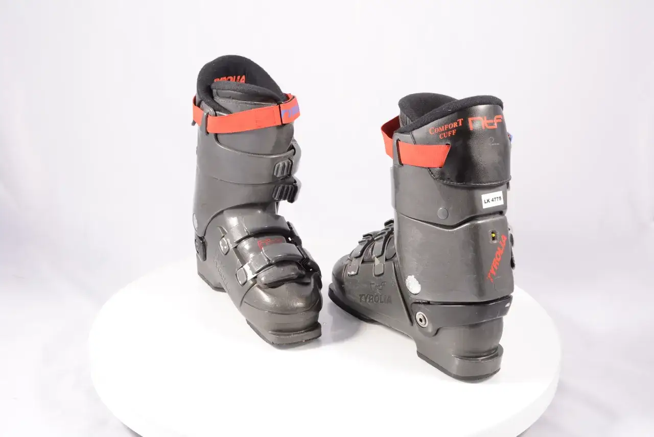 Dwa ciemnoszare buty narciarskie z czerwonymi ramiączkami i logo Tyrolia.