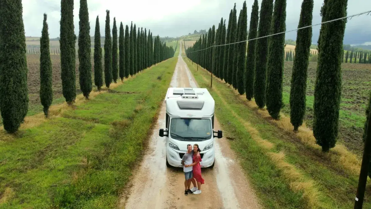 Para podróżuje kamperem do Włoch, zatrzymując się na malowniczej drodze otoczonej cyprysami.