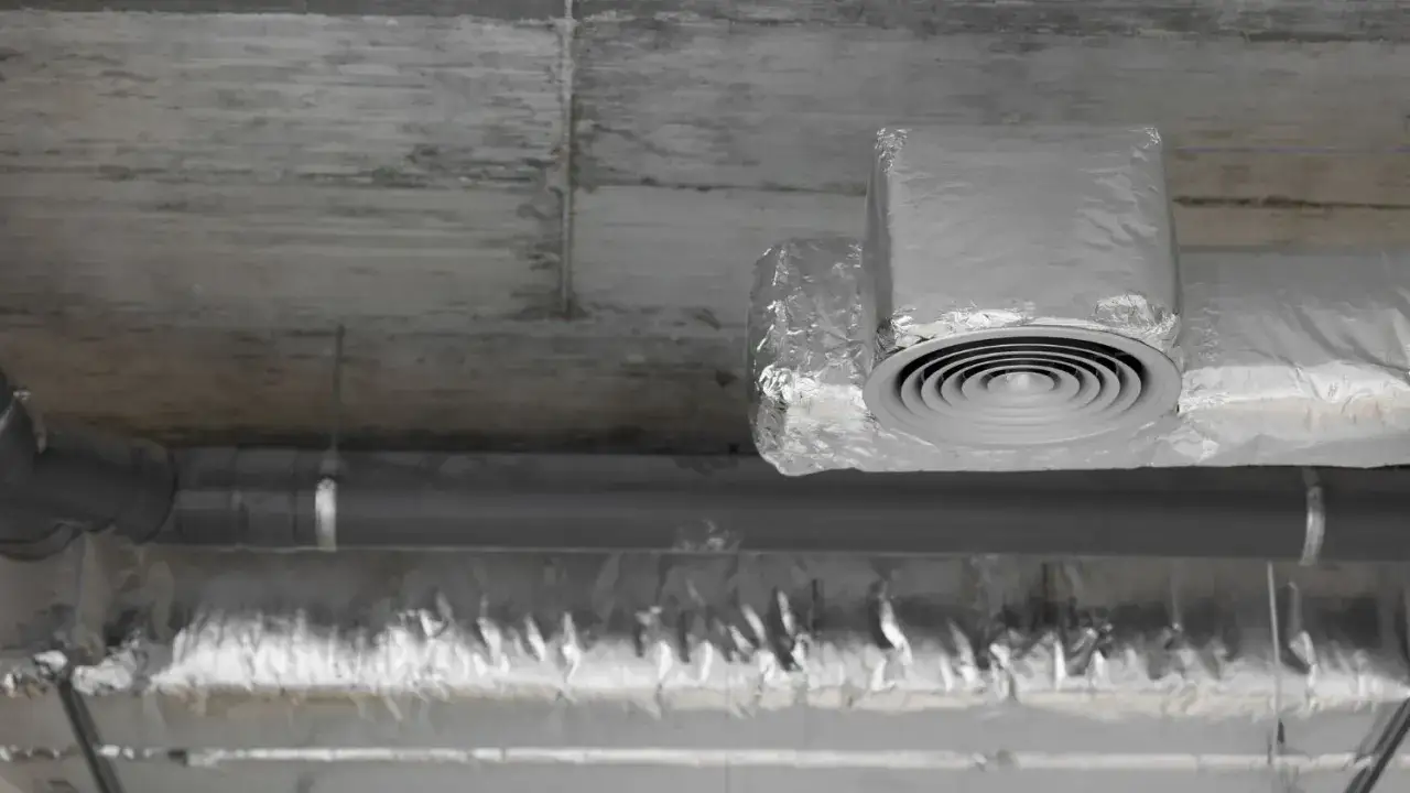 Izolowane rury wentylacyjne z okrągłym nawiewnikiem pod betonowym sufitem.