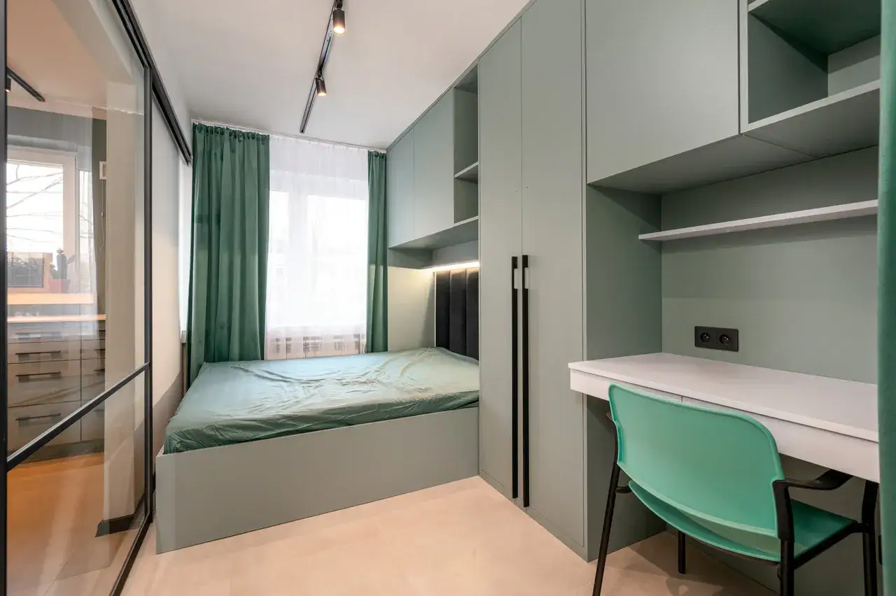 Nowoczesny styl sypialni z łóżkiem, biurkiem i szafami w odcieniach zieleni. Wygodne miejsce do odpoczynku i pracy.