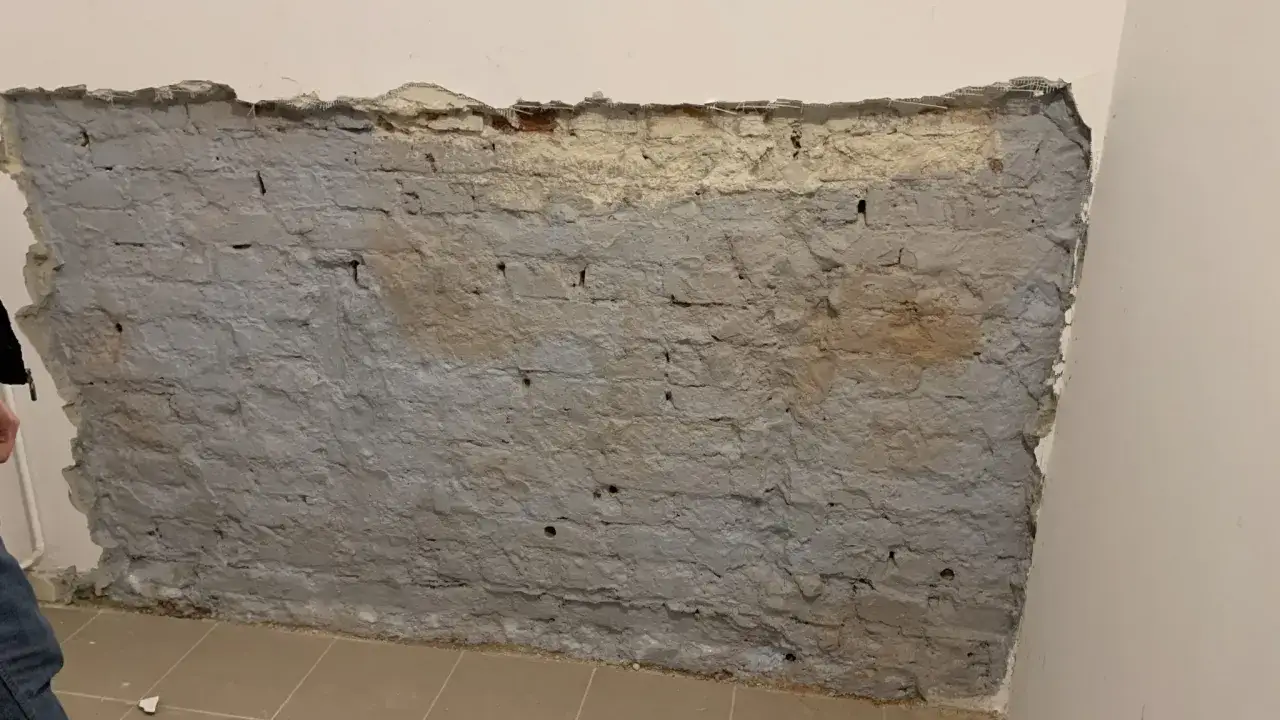 Fragment odsłoniętej, starej ceglanej ściany z szarym tynkiem i fragmentami żółtego podkładu.