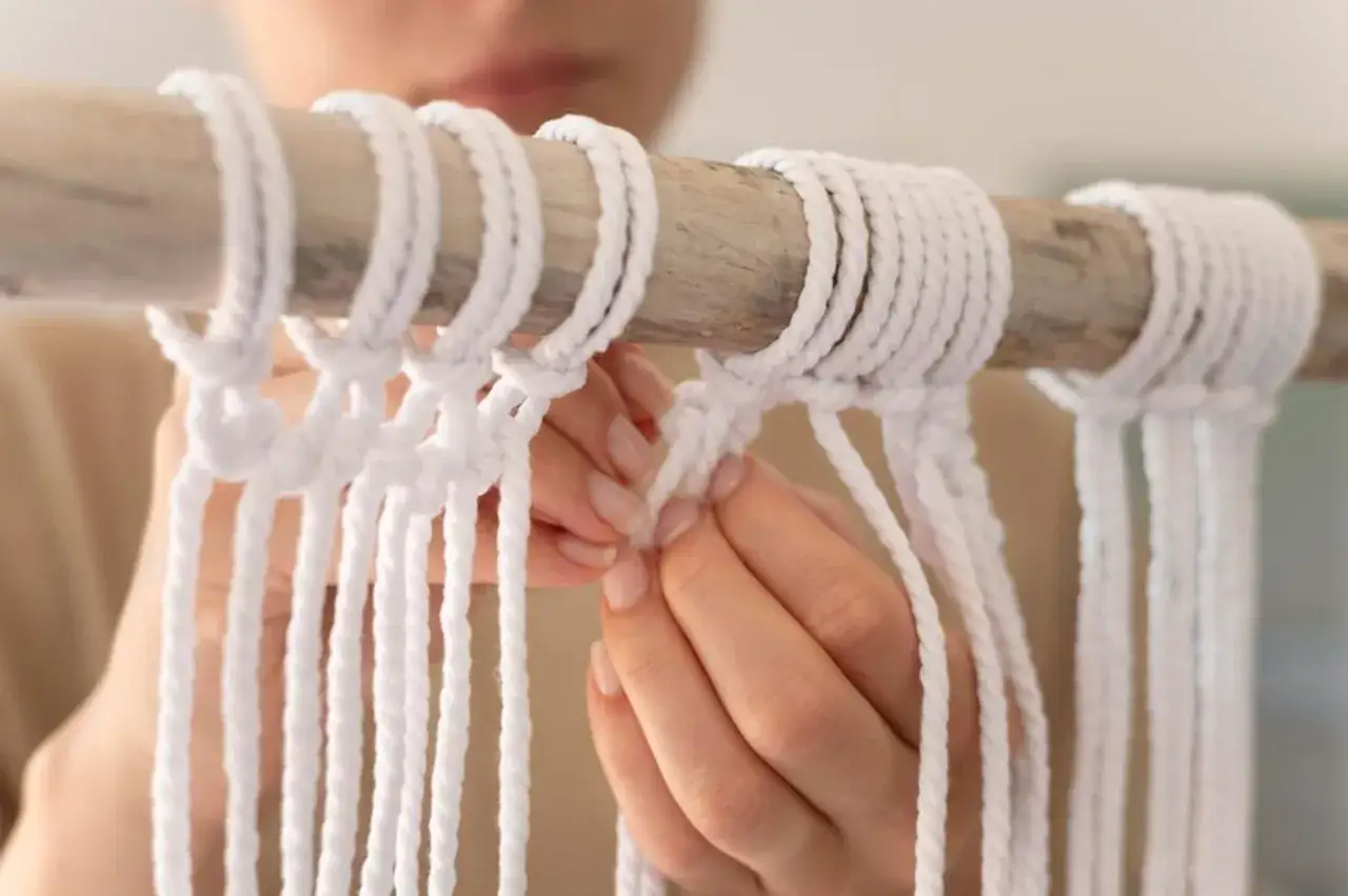Dłonie tworzą wzory z białego sznurka na drewnianym kiju. Idealny sznurek do bransoletek z makramy.
