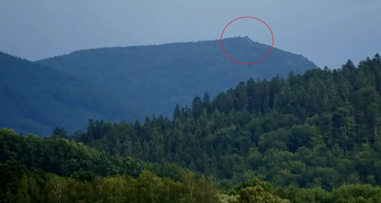 Górzyste krajobrazy czeskich Izery, z zalesionymi zboczami i skalistym szczytem zaznaczonym czerwoną obwódką.