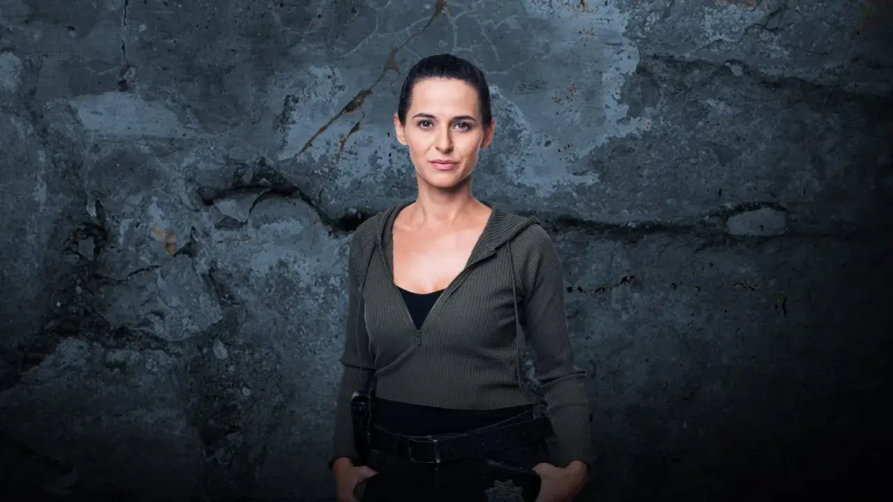 Natalia Brudniak w wojskowym stylu, z rękami w kieszeniach, na tle zniszczonej ściany.