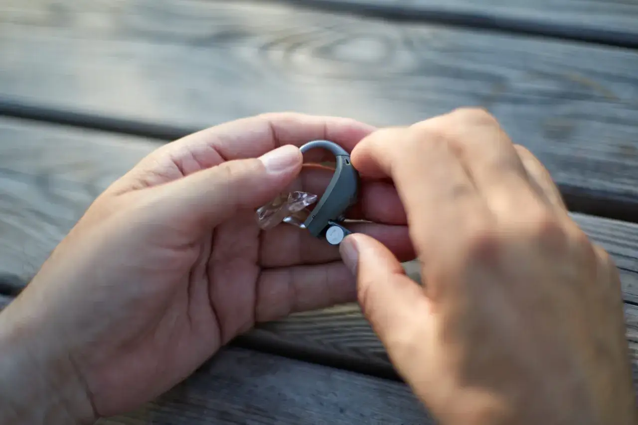 Dłonie trzymają aparat słuchowy, pokazując, dlaczego baterie w aparacie słuchowym szybko się wyczerpują.