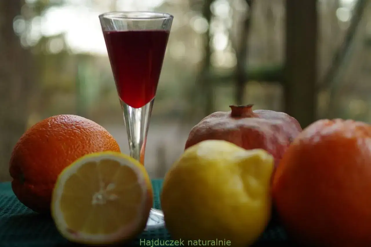 Szklanka z czerwonym napojem, obok pomarańcze, cytryna i granat. Czy to grenadyna? Hajduczek naturalnie.