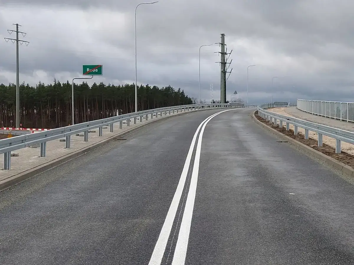 Droga ekspresowa jednojezdniowa z podwójną białą linią, znakiem Ruda i barierami ochronnymi.