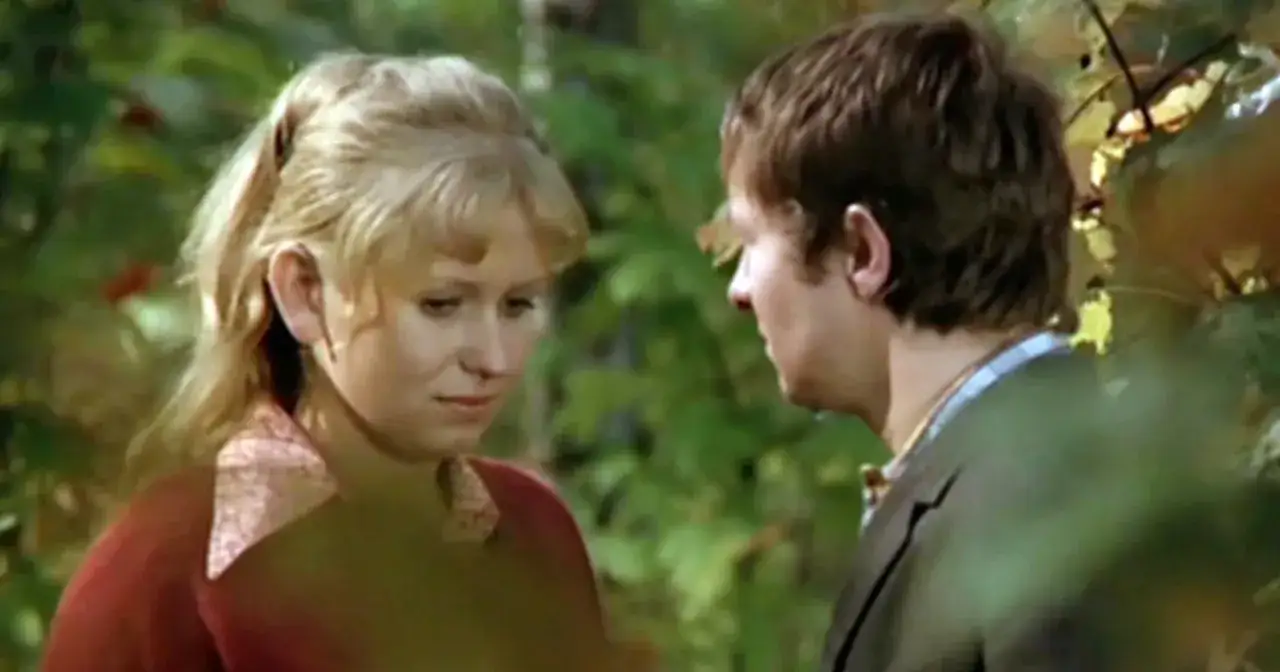 Irena Hrehorowicz w otoczeniu zieleni, spogląda w dół, rozmawiając z mężczyzną.