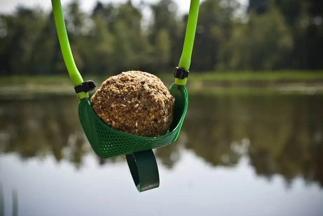 Zielona proca do zanęty z kulką zanętową gotowa do rzutu nad spokojną wodą.