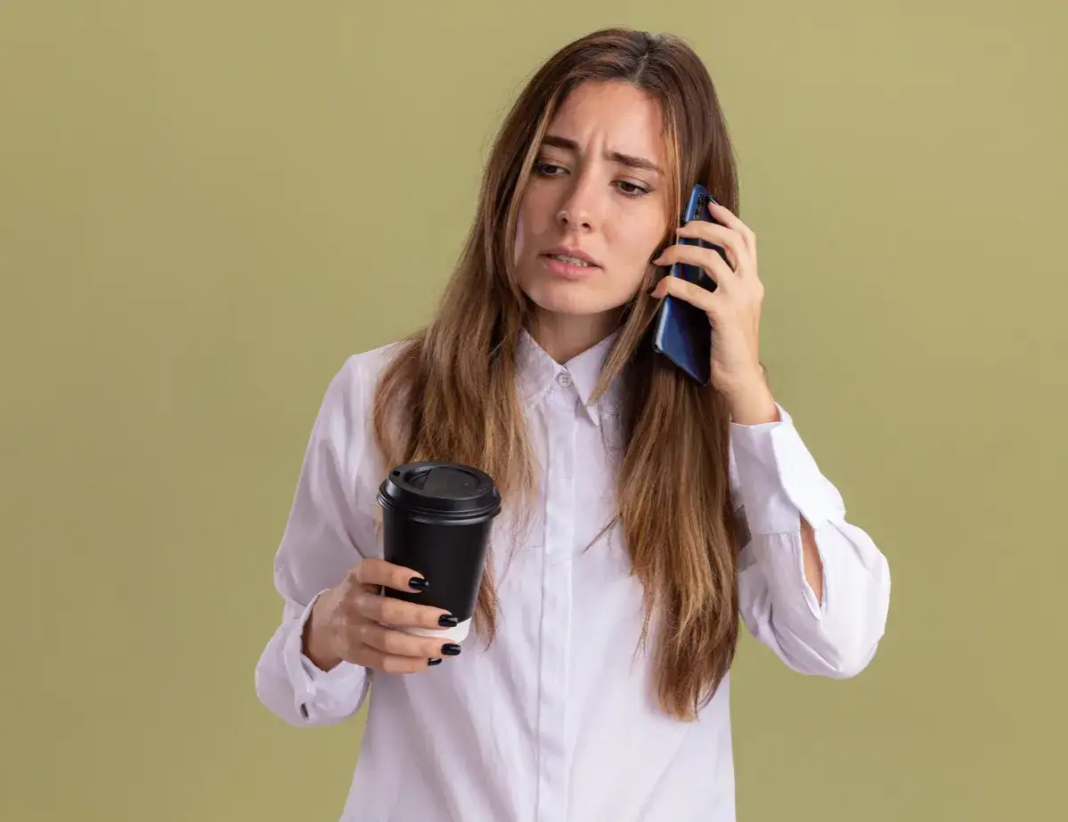 Zmartwiona kobieta z kawą w ręku rozmawia przez telefon, zastanawiając się, dlaczego nikt nie dzwoni po wysłaniu CV. Najczęstsze błędy w dokumentach.