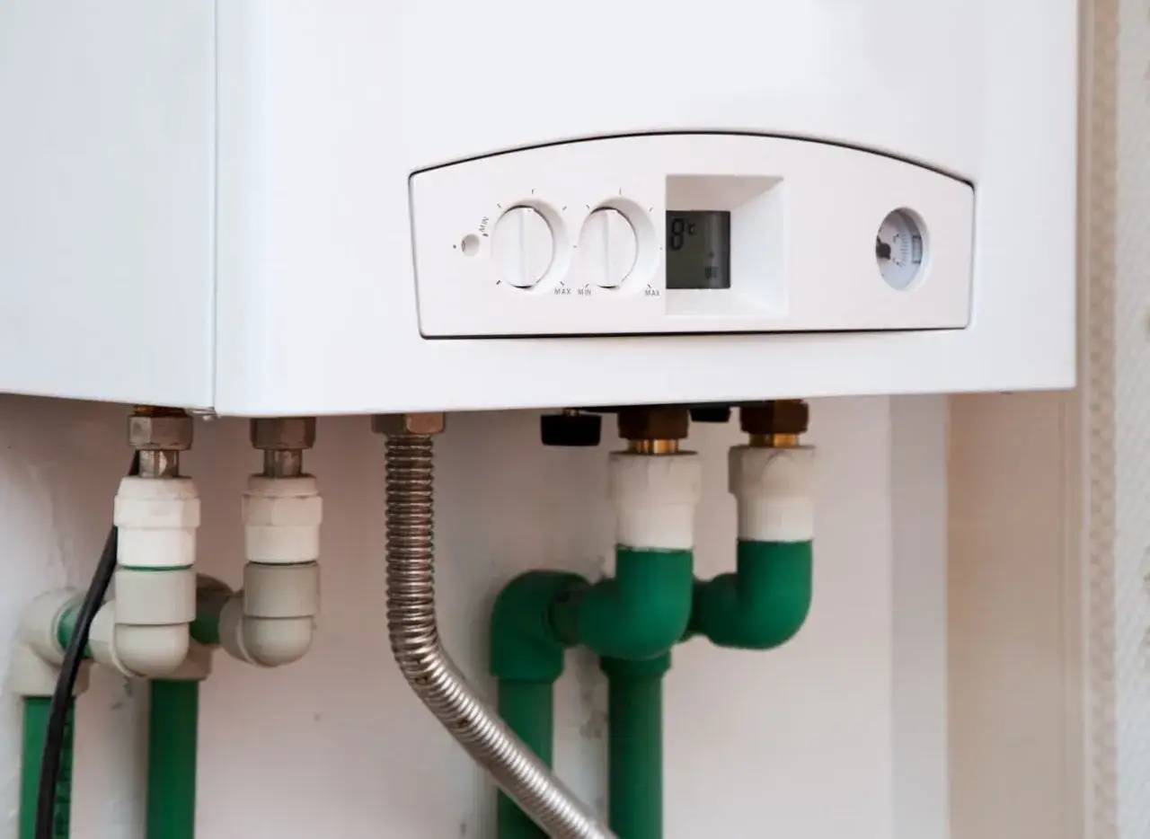 Jaki piec gazowy do domu 120m2? Biały kocioł gazowy z cyfrowym wyświetlaczem i pokrętłami regulacji, podłączony do zielonych rur.