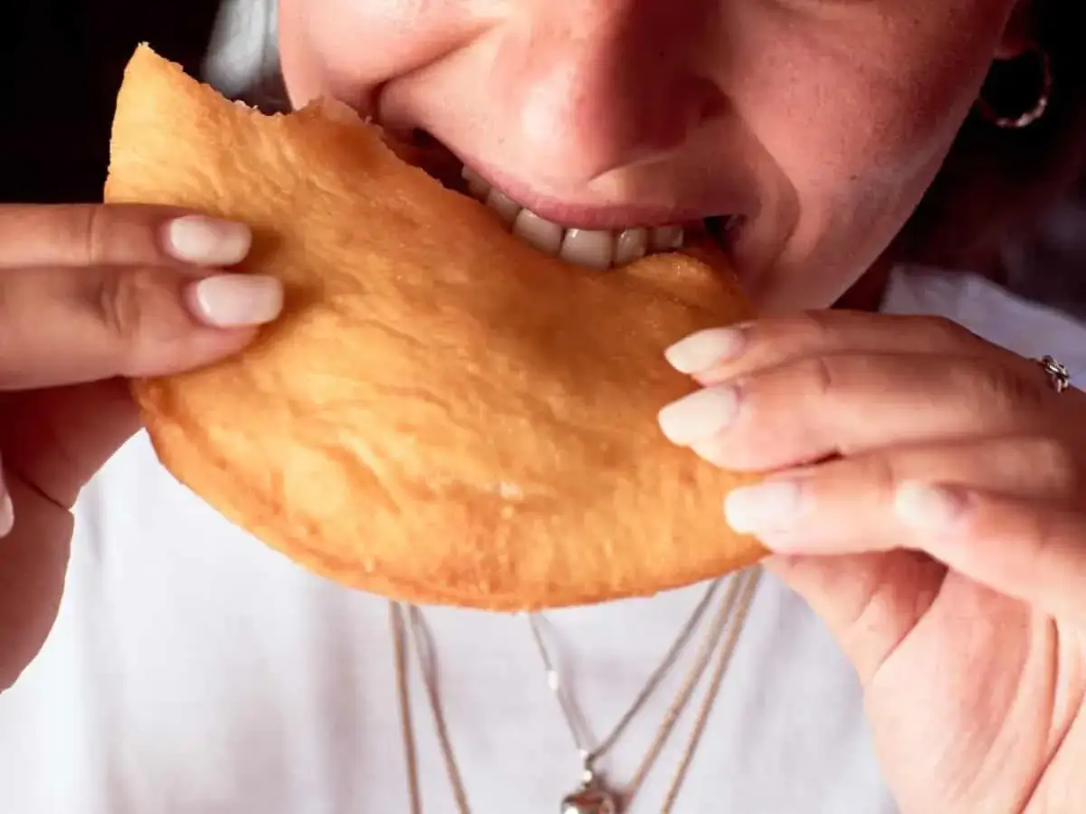 Close-up of a person biting into a golden-brown, fried pastry.
