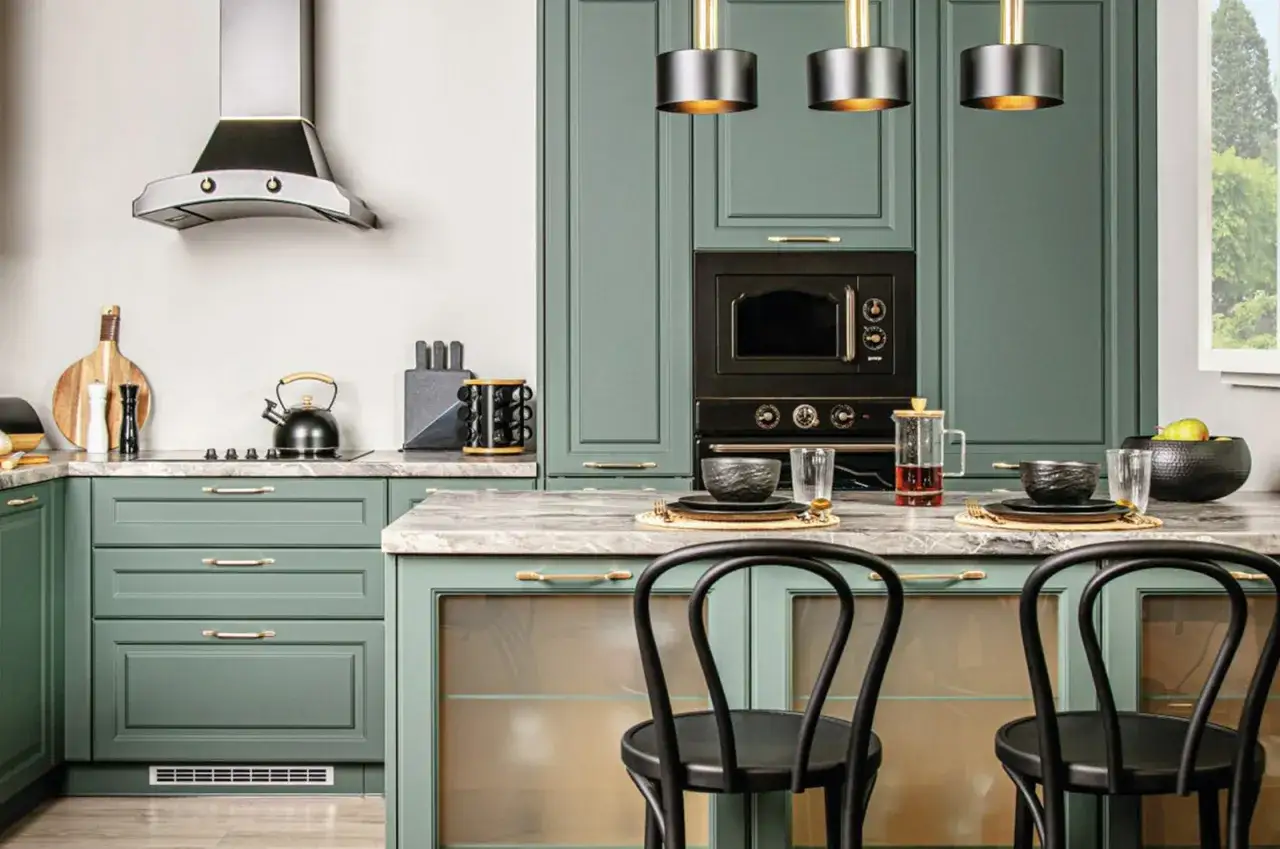 Nowoczesna kuchnia z zielonymi frontami, złotymi uchwytami i czarnymi krzesłami barowymi.
