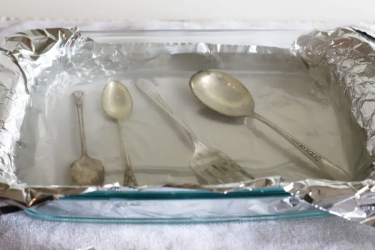 Srebrne sztućce w szklanej misce wyłożonej folią aluminiową.