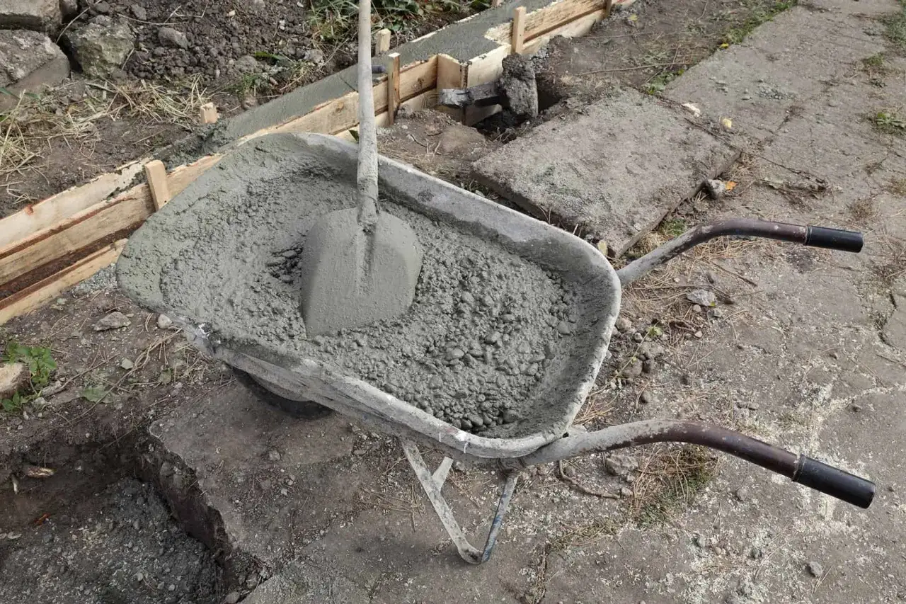 Taczka z betonem i łopatą czeka na wylanie zbrojenia ławy fundamentowej.