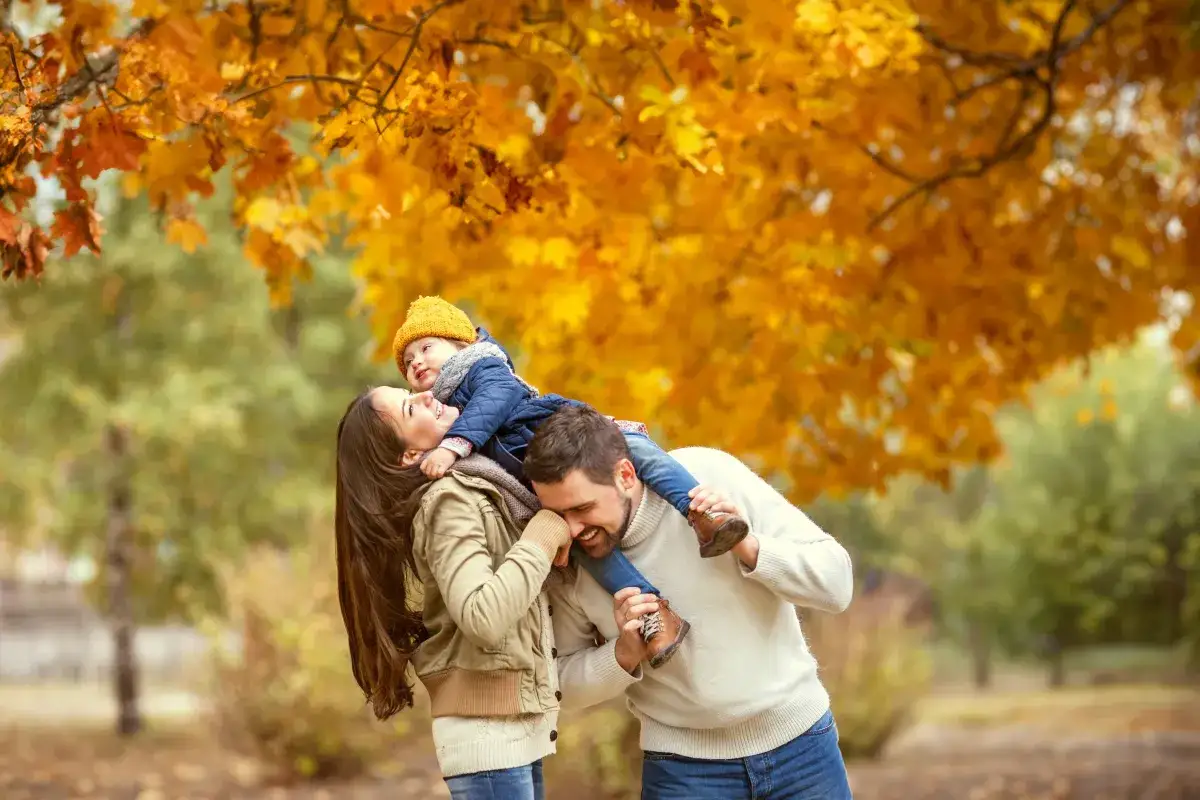 Rodzina ciesząca się jesiennym spacerem pod drzewem w złotych liściach.