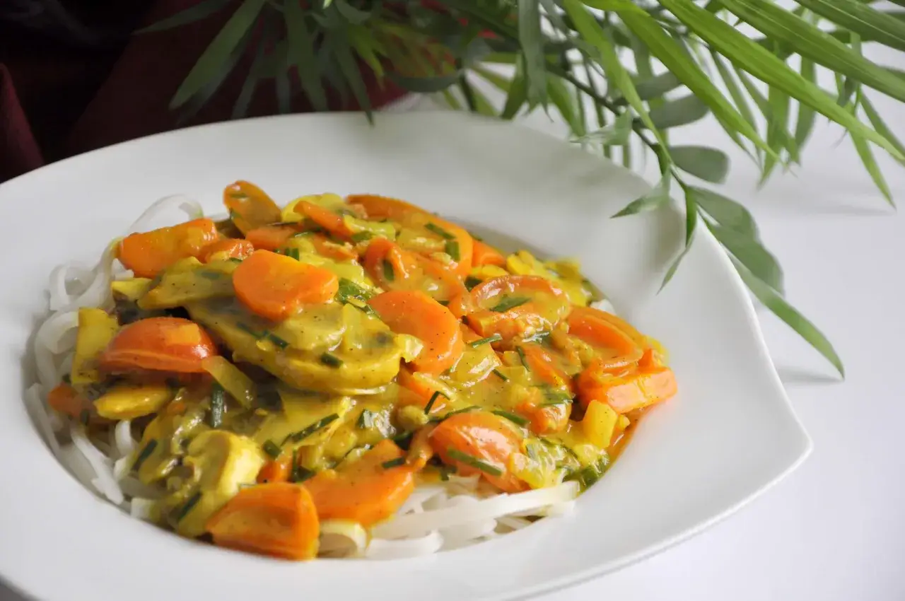 Zdrowy obiad: makaron ryżowy z warzywami w sosie curry. Kolorowe marchewki i inne warzywa tworzą apetyczną kompozycję.