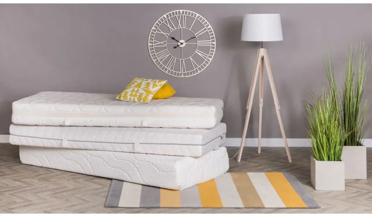 Stos piankowych materacy z poduszkami, lampą i zegarem na ścianie.