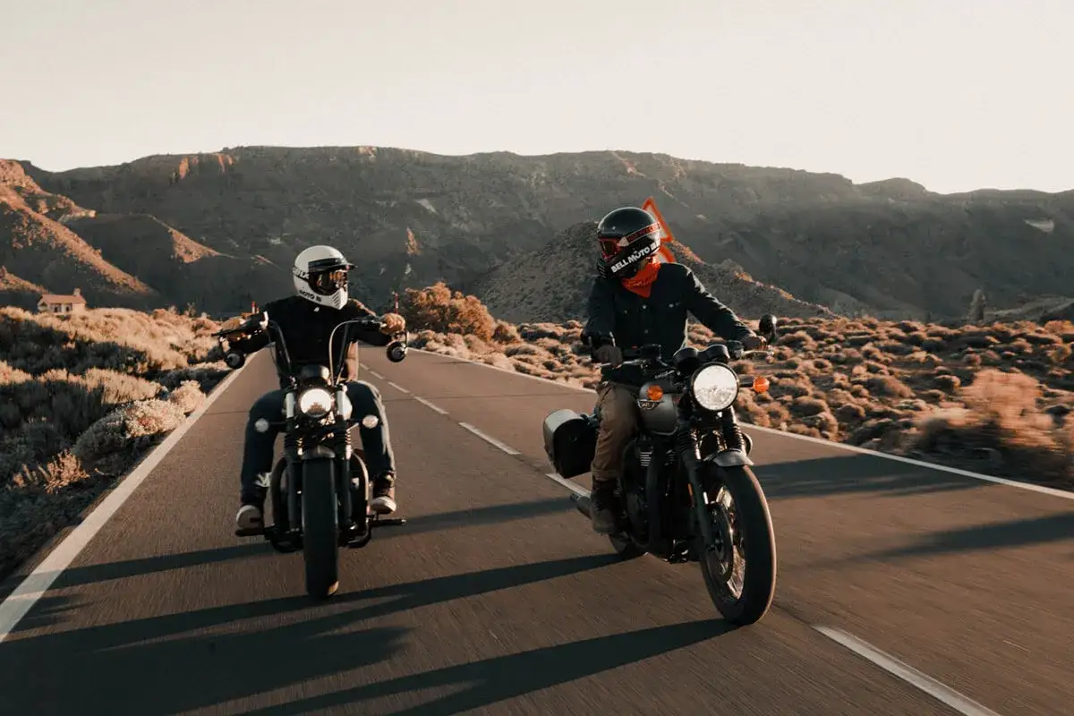 Dwóch motocyklistów w stylowym ubraniu na motor turystyczny przemierza pustynną drogę.